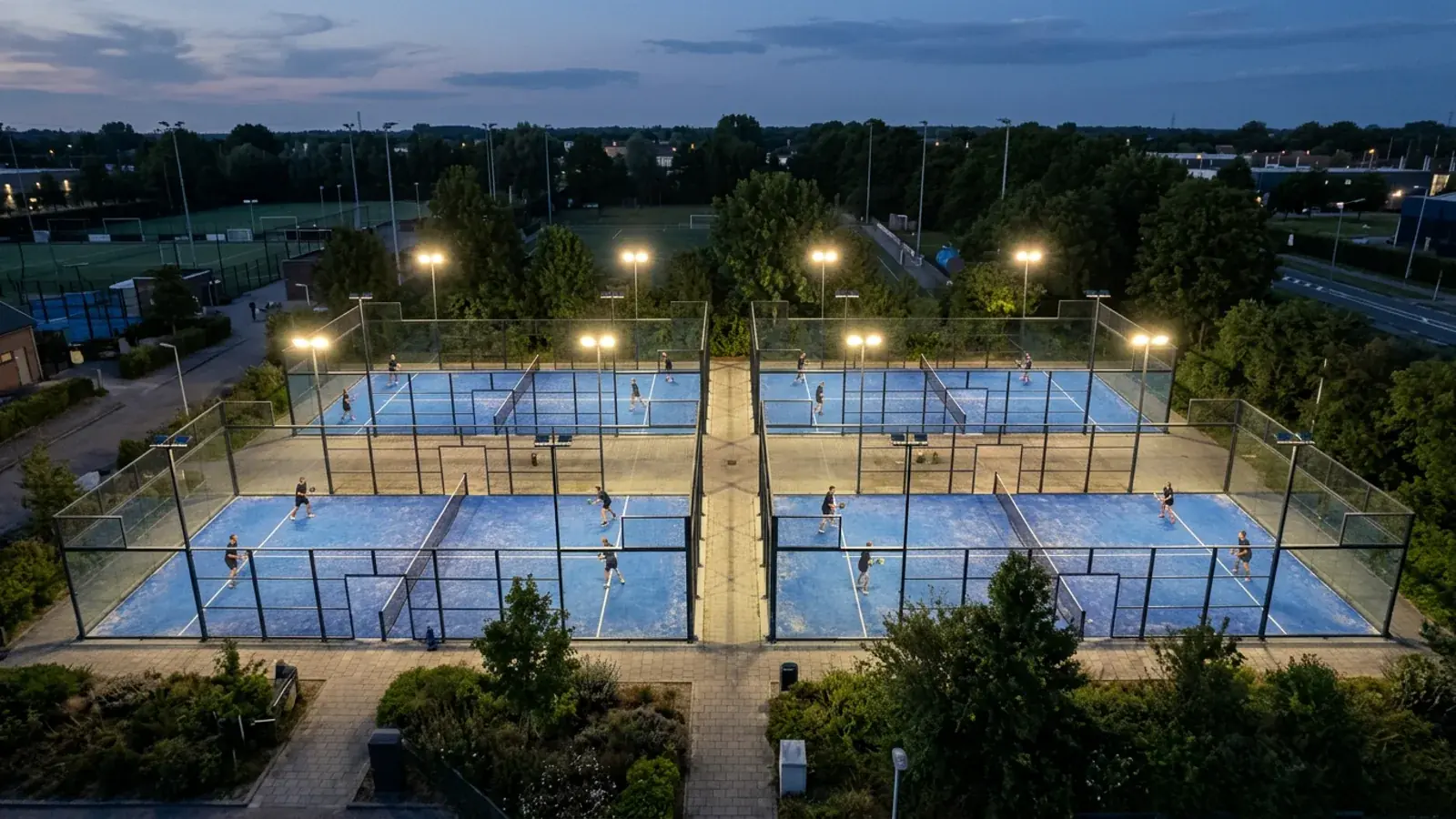 Vier Padel-Courts am Abend von oben, alle Plätze belegt, Flutlicht an